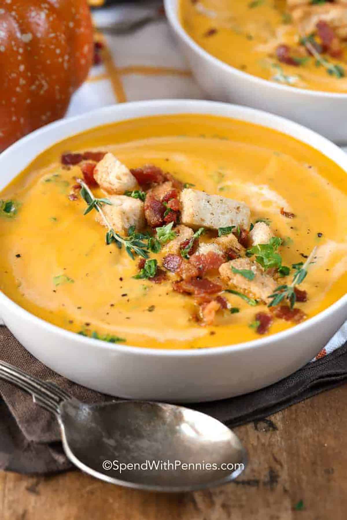 This creamy pumpkin soup is sure to become a fall favorite, with its savory sweet flavors and delicious bacon topping. It's easy to make, and it's easy to switch ingredients to make a different-styled soup. Try a Thai inspired soup with coconut cream and curry, or cook it with sweet potato or butternut squash added in. So many options for this cozy bowl! #pumpkinsoup #recipeeasy #withcannedpumpkin #spendwithpennies bowl of Pumpkin Soup with croutons and bacon