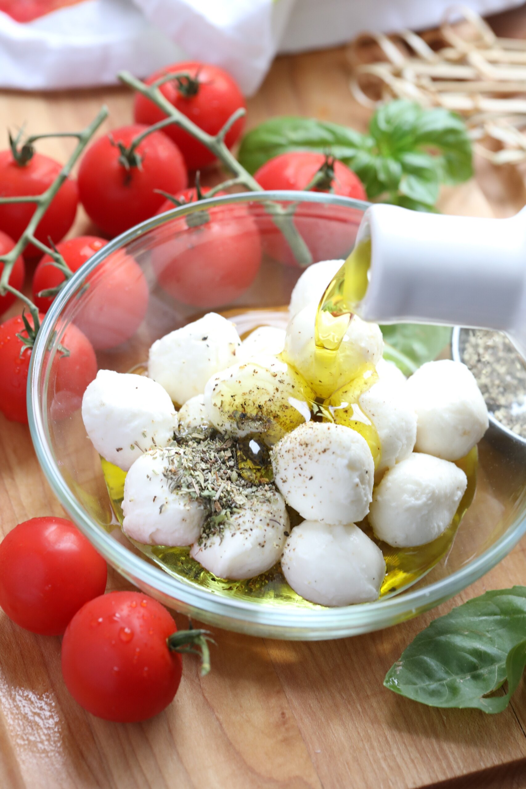 This Caprese skewer recipe is perfect for parties. It’s a popular combination of cherry tomatoes, olive oil marinated mozzarella balls, and fresh basil. These easy skewers are a quick, healthy, low carb appetizer that everyone loves! #spendwithpennies #capreseskewers #caprese #appetizer pouring oil over cheese and seasonings to make Caprese Skewers