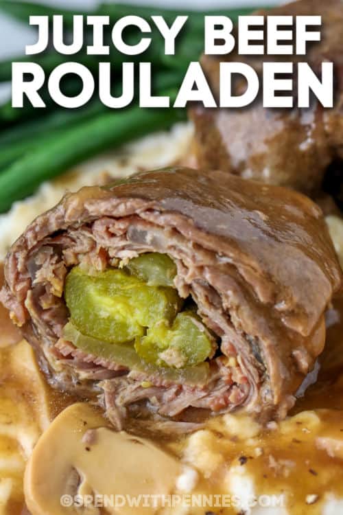 Rouladen is a classic German dish made with thinly sliced inside round or flank steak. The Rouladen meat is then topped with pickles, mustard, onions, and bacon before being baked in the oven. This recipe takes time to cook but it is worth the wait! #spendwithpennies #rouladen #maincourse #beefrecipe close up of Beef Rouladen on mashed potatoes with writing