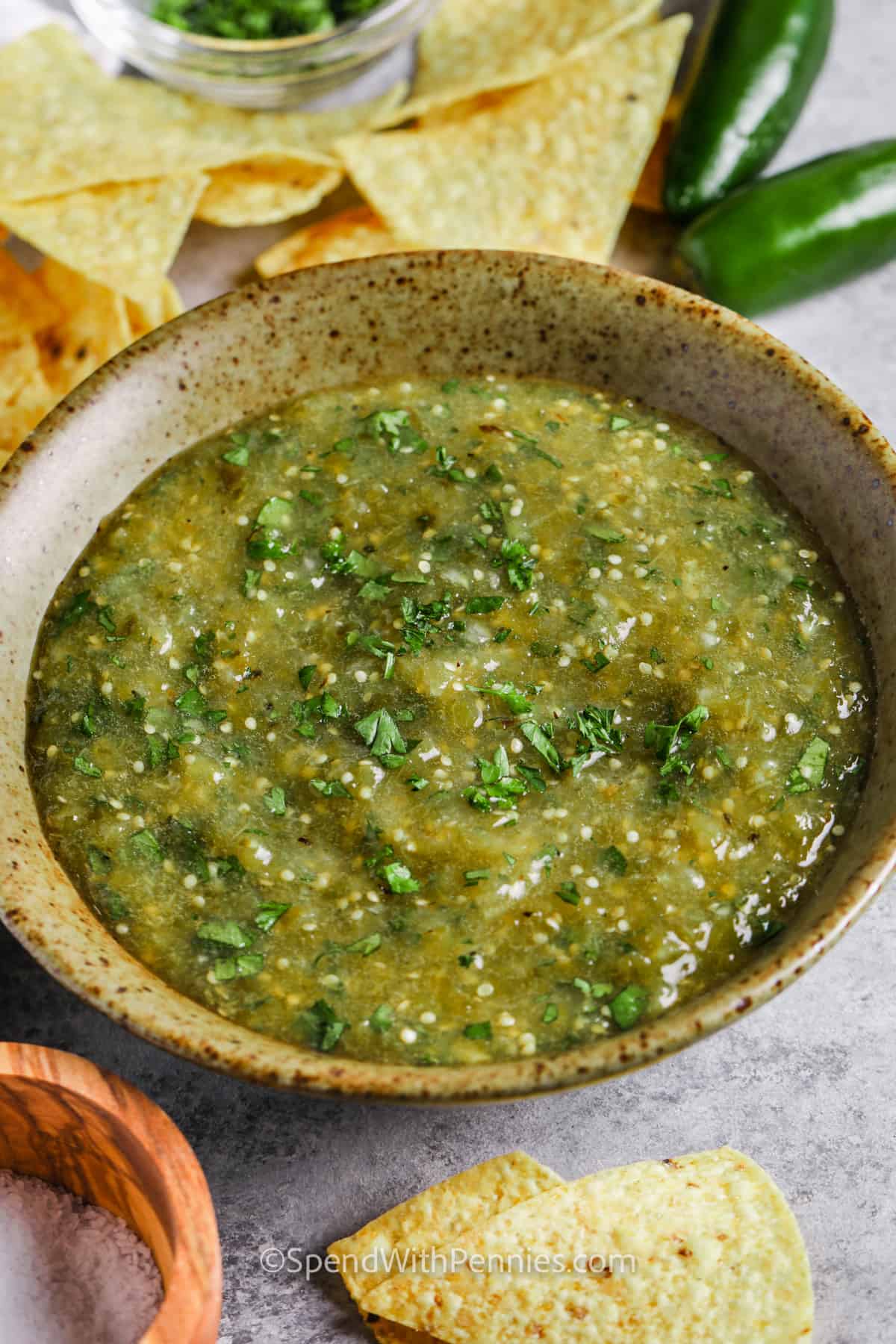 This tangy salsa verde recipe gets its bright and zesty flavors from all fresh ingredients! Tomatillos and green serrano or jalapeno peppers are roasted under an oven broiler, then popped in the food processor with onion, garlic, and cilantro. It’s the perfect condiment for tacos, enchiladas or chili con carne! Why buy salsa verde from a jar, when you can make it quick and easy, with no preservatives? #salsaverde #spendwithpennies #salsaverderecipe #mexicansalsaverde plated Salsa Verde with chips