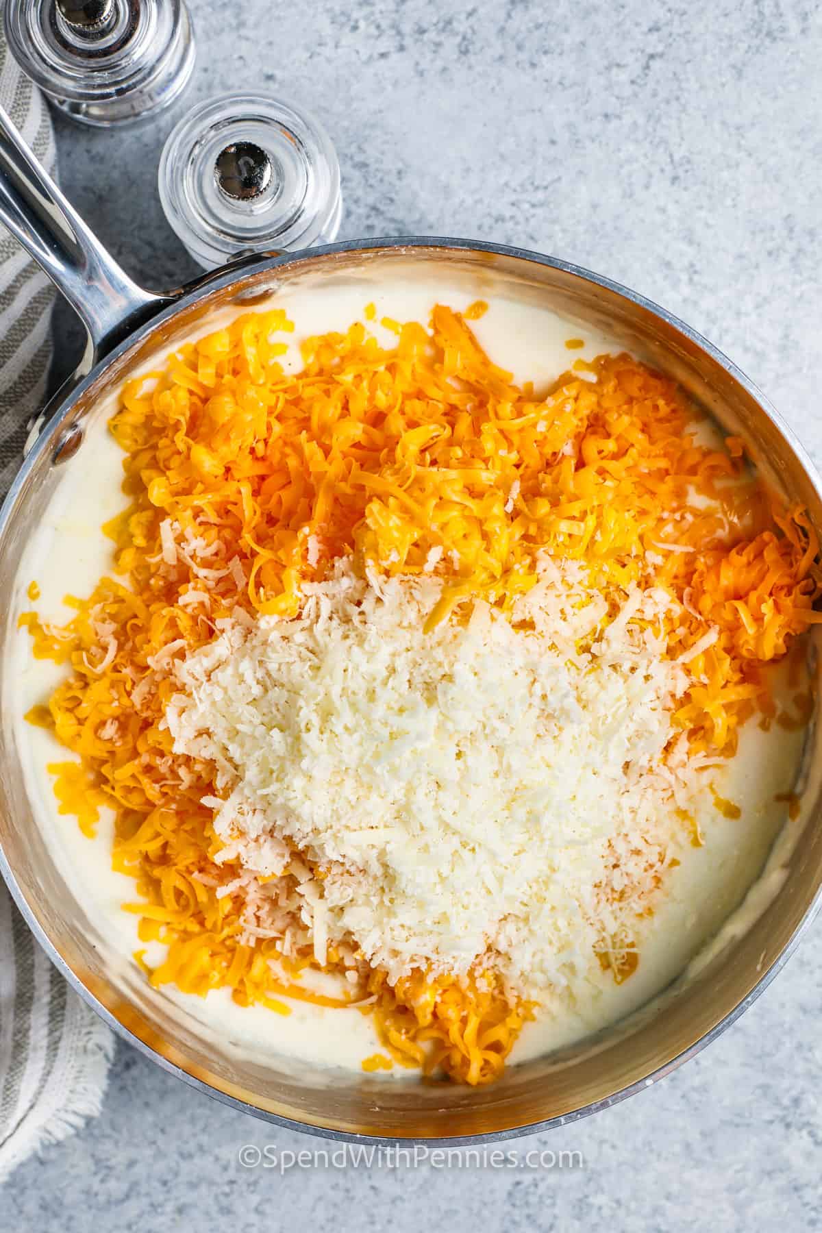 This baked mac and cheese dish is classic comfort food that everyone enjoys. It's perfect for potlucks or as a family entree. Creamy and delectable, this oven-baked casserole features three cheese varieties, milk, and cream, creating a decadent homemade meal that's always a favorite. #bakedmacandcheeserecipe #homemademacandcheese #creamymacandcheese #spendwithpennies adding cheese to pot to make Baked Mac and Cheese