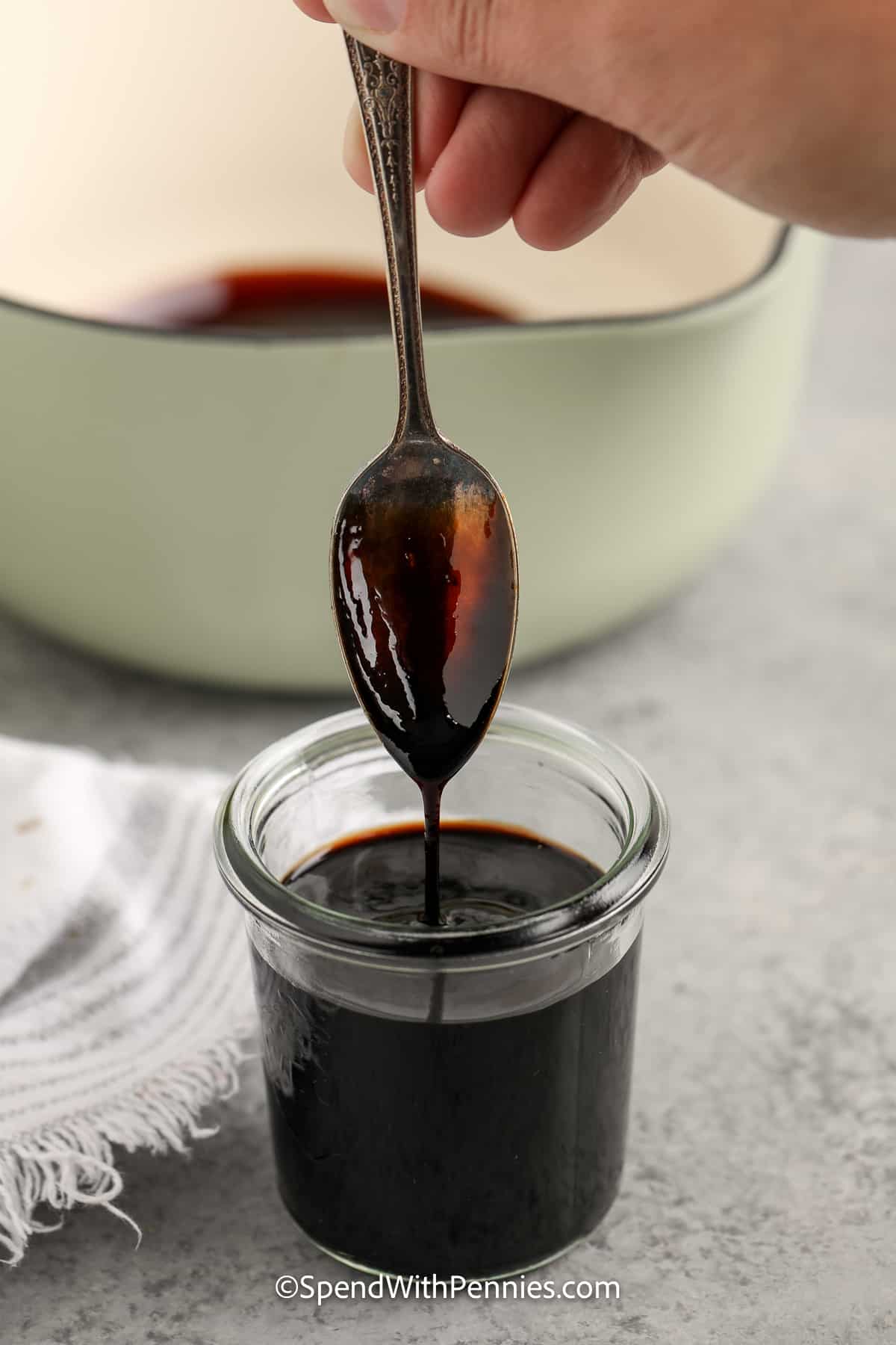 Make this simple balsamic glaze recipe and enjoy using it on pork, salmon, steak, or chicken. It's also delicious drizzled on grilled or roasted vegetables like carrots, Brussels sprouts, asparagus, or broccoli. Make a double batch of this easy two-ingredient recipe, and enjoy it on so many favorite dishes, or to enhance a special meal. #balsamicglaze #balsamicglazerecipe #homemadebalsamicglaze #spendwithpennies balsamic in a small jar with a spoon