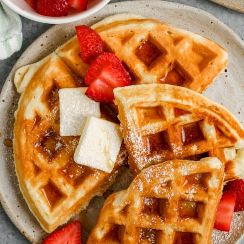 belgian waffles on a plate topped with butter, syrup, and strawberries