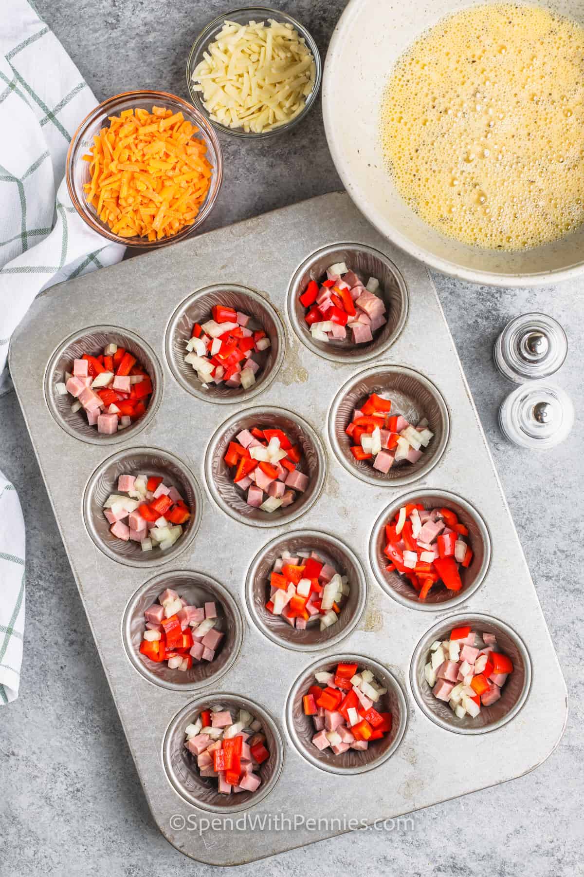 Egg Muffins are a delicious & tasty make-ahead meal. Naturally low-carb & easy to make ahead, these egg cups are perfect for an on-the-go breakfast! Add your fave meat and veggies and make them different every time! #eggmuffins #makeahead #breakfast #spendwithpennies adding ham and vegetables to muffin tin to make Make Ahead Egg Muffins