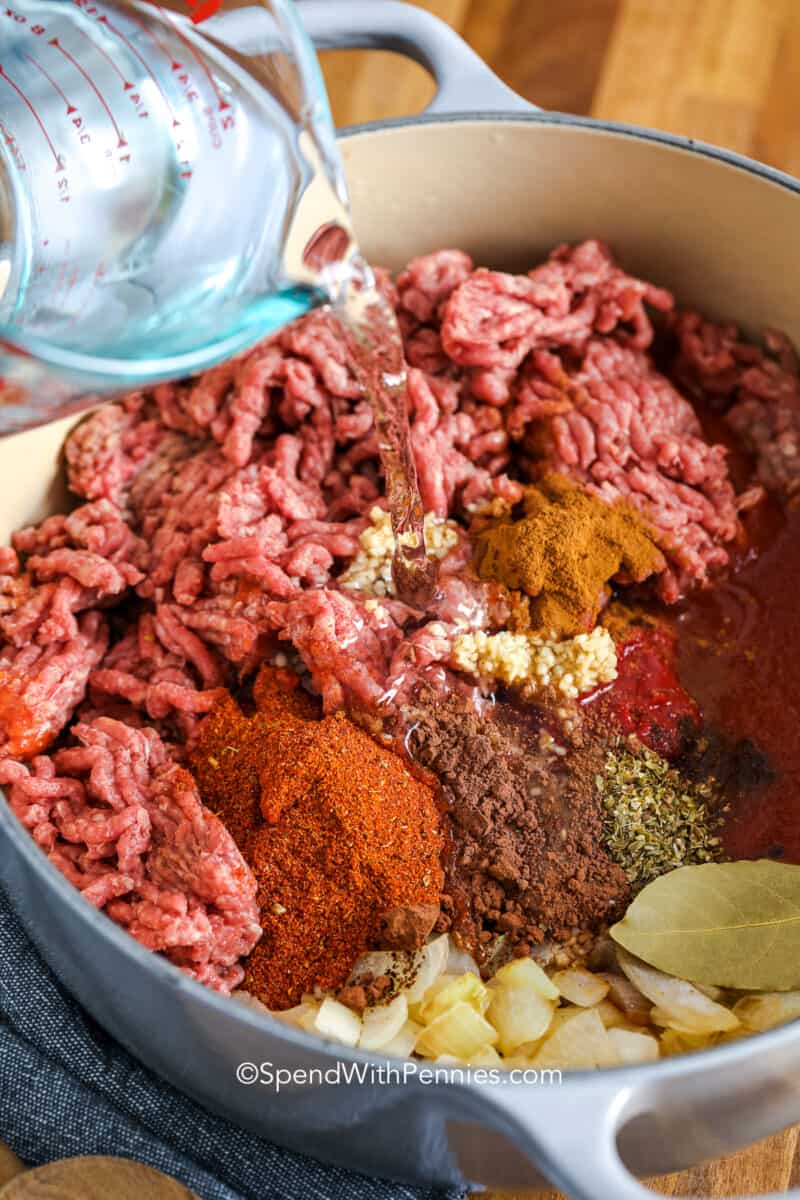 adding water to uncooked ingredients for cincinnati chili in a dutch oven