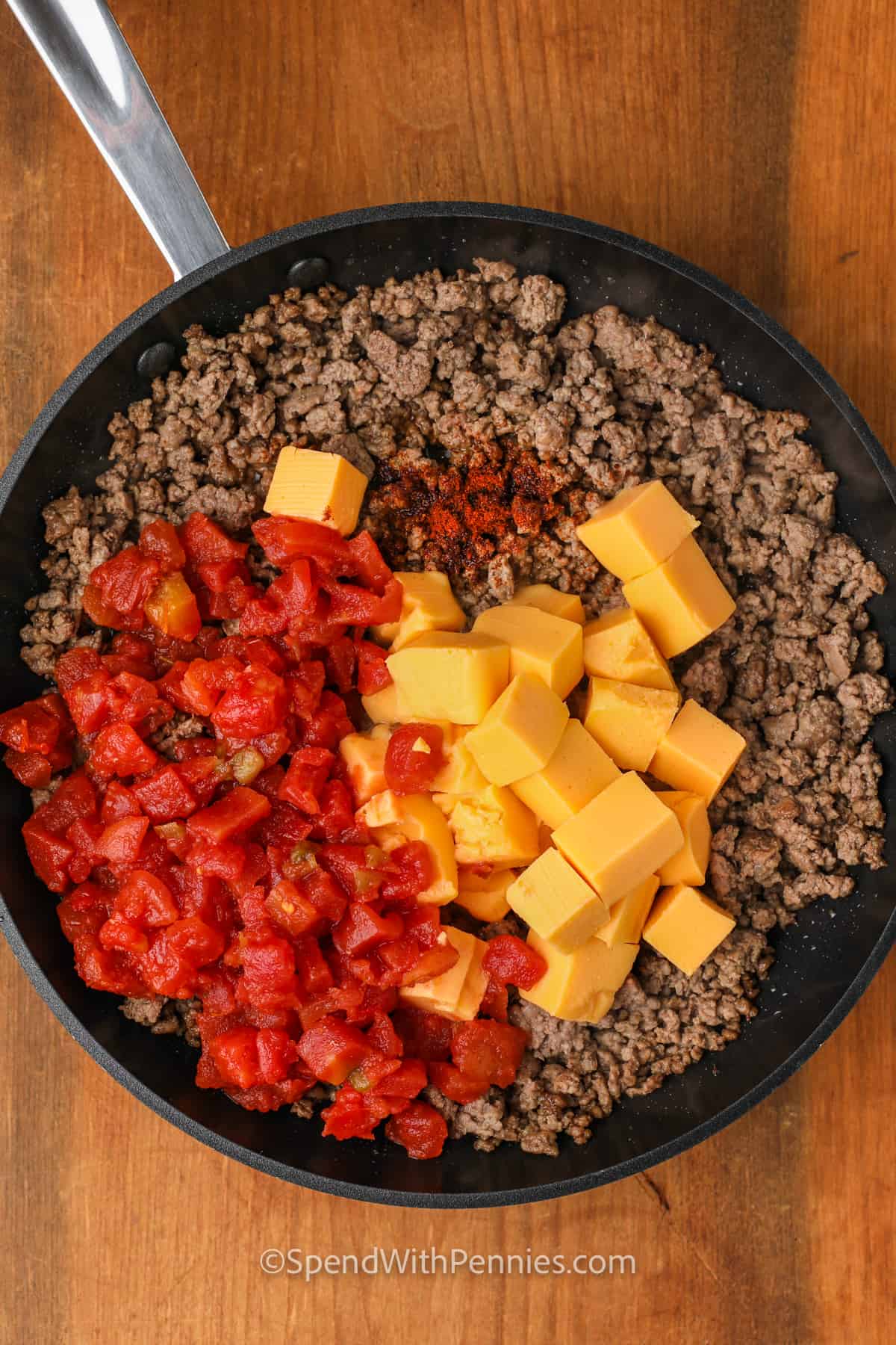 This easy cheesy Rotel dip is ready in 20 minutes and made with just 4 simple ingredients. We add ground beef or sausage to create a hearty party favorite. Serve with an assortment of dippers for the perfect appetizer or party spread. #roteldip #velveetadip #groundbeefdip #spendwithpennies adding ingredients to cooked beef to make Rotel Dip