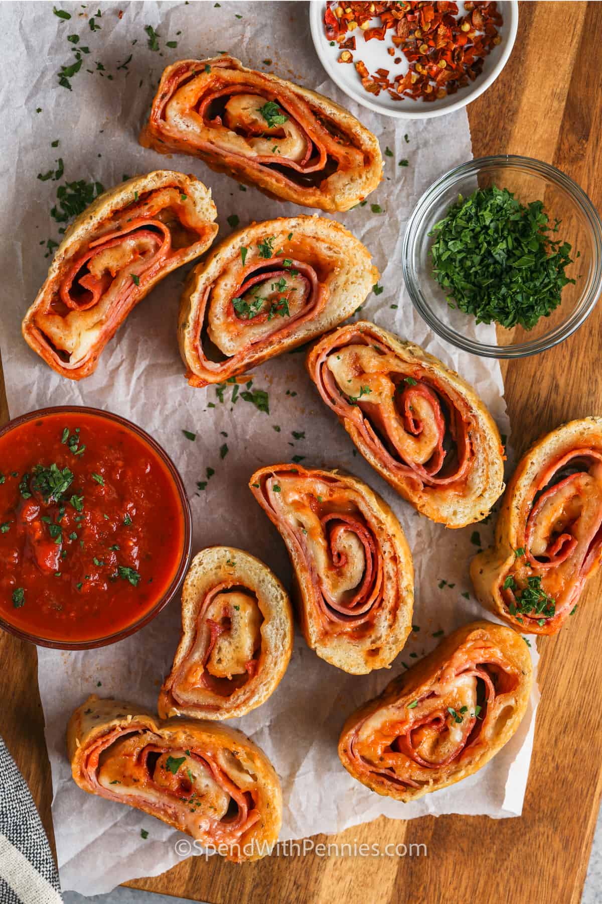 Slice and serve this homemade stromboli recipe with an extra helping of tasty sauce for dipping. Anyone who loves Italian food will love this easy recipe, and it's ready in half an hour! This easy stromboli uses refrigerated pizza dough to keep it simple. Roll it up with salami, pepperoni, ham, and plenty of cheese. #easyhomemaderecipes #italianstromboli #strombolirecipe #spendwithpennies sliced Stromboli Recipe with garnish and dips