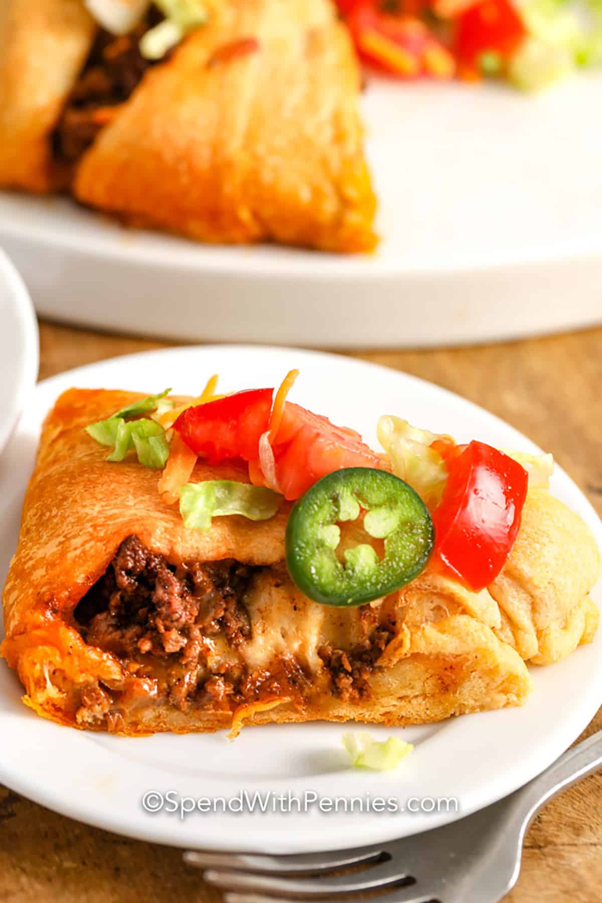 This taco ring recipe is beefy, crunchy, and so easy to prepare. Made with crescent rolls, seasoned beef, and delicious seasonings, this party appetizer is always a hit! Set out the toppings in bowls and let everyone choose their faves, this appetizer won't disappoint! #tacoring #tacocrescentring #appetizer #spendwithpennies sliced Taco Ring on a plate