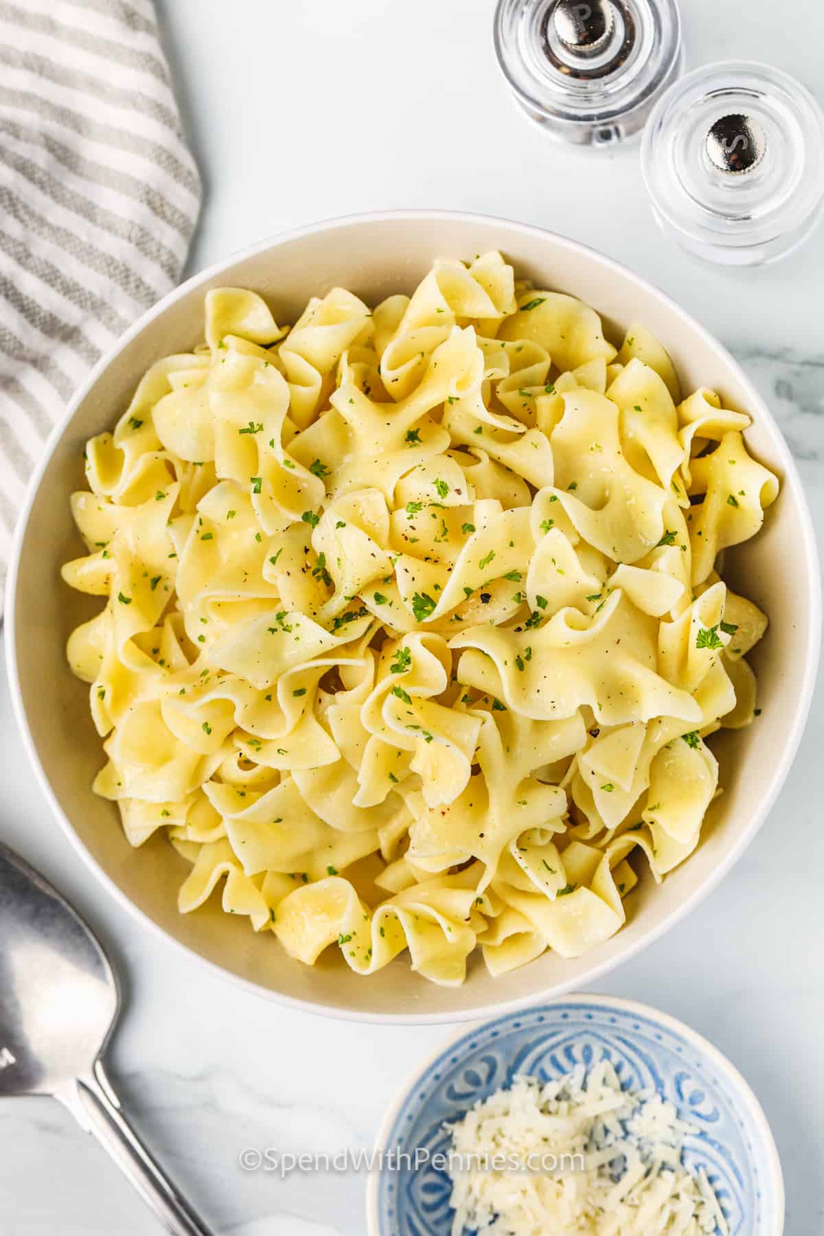 Buttered noodles are the ultimate comfort food, with tender egg pasta coated in melted butter and a touch of garlic powder and other seasonings. This simple stovetop recipe is easy to season just the way you like, with fresh parsley and a sprinkle of Parmesan for richness. Serve it as a plain side or dress it up with your favorite toppings for the best homemade pasta dish that pairs with almost anything. #spendwithpennies top view of Buttered Noodles in a bowl