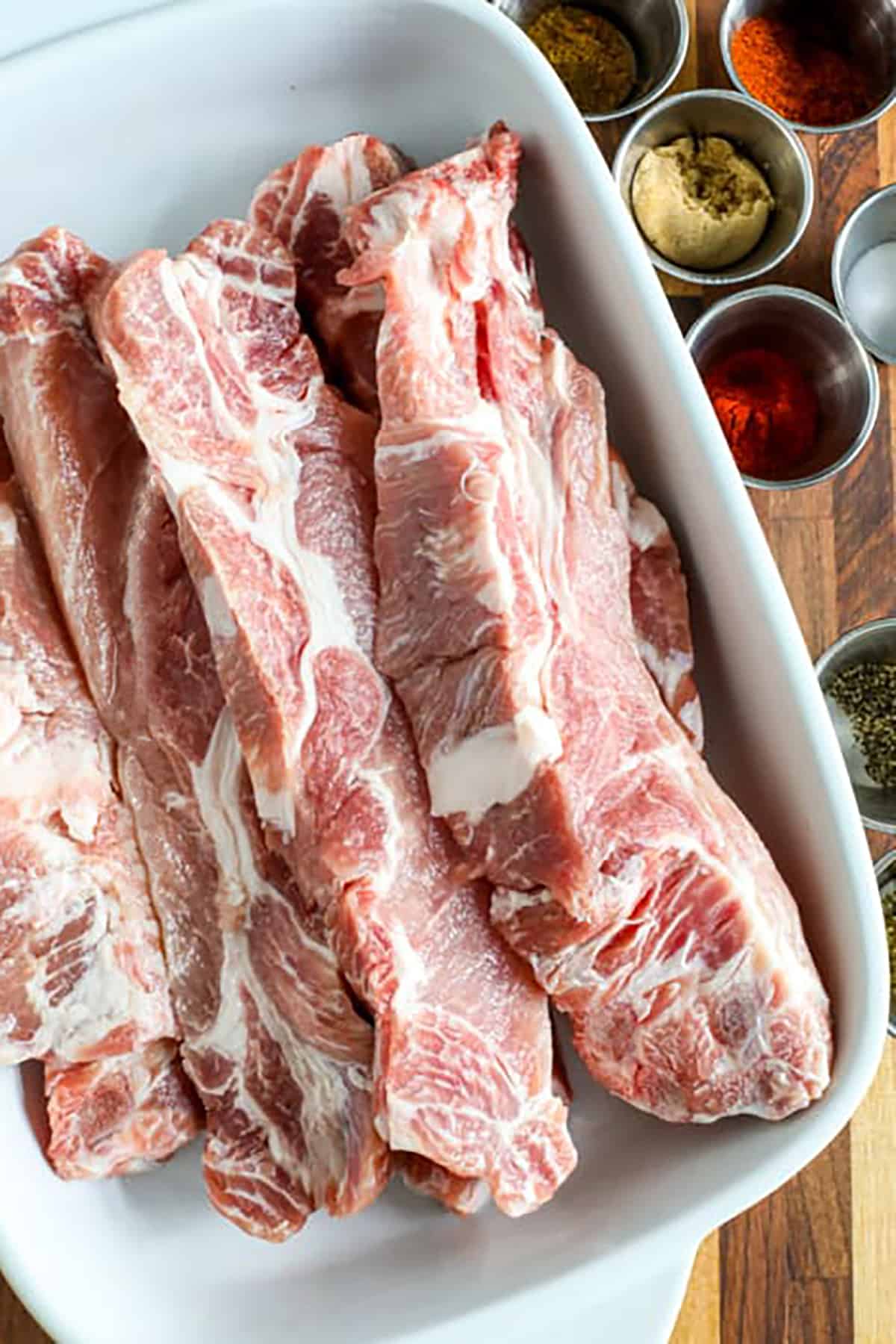 Treat your family to the delicious, smoky flavors of country style ribs! These ribs are seasoned with a homemade rub, slow-cooked until tender, and finished with a generous brushing of barbecue sauce. The result is a rich, hearty dish that’s perfect for any occasion. Whether you’re cooking for a weeknight dinner or a special gathering, these ribs are sure to impress. Serve with your favorite sides and enjoy a meal everyone will love! #spendwithpennies ribs in a dish with seasonings in bowls to make BBQ Country Style Ribs