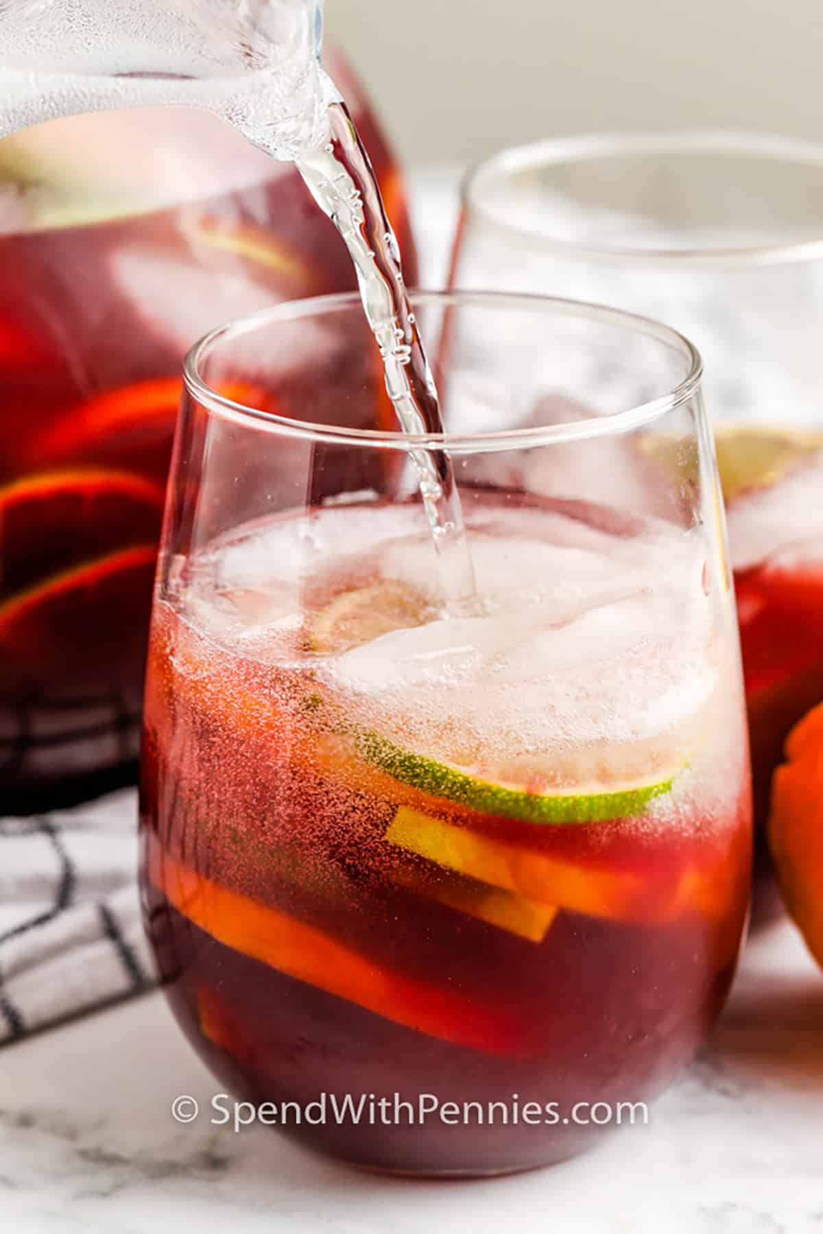 Make this quick and easy red sangria recipe for the best summer sipper ever! It is ready to enjoy in just two easy steps and it's best made ahead of time so it's perfect to serve guests! It goes great with tapas (Spanish small plates) and other bold-flavored foods because of its light and refreshing, sweet, and fruity taste! #redsangriarecipe #redsangria #redwinesangriarecipe #spendwithpennies adding club soda to glass to make Easy Red Sangria