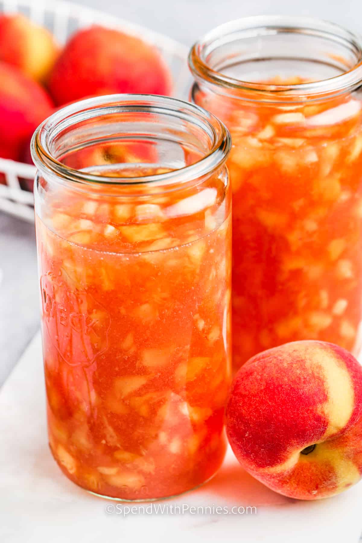 Learn how to make an easy freezer peach jam with this simple recipe. When peaches are in season try making freezer jam! All that is needed is sweet delicious peaches, some pectin, sugar, and a little lemon juice. This recipe makes canning so easy and effortless! #peachjam #freezerjam #peachfreezerjam #spendwithpennies Peach Freezer Jam in jars with peaches beside it