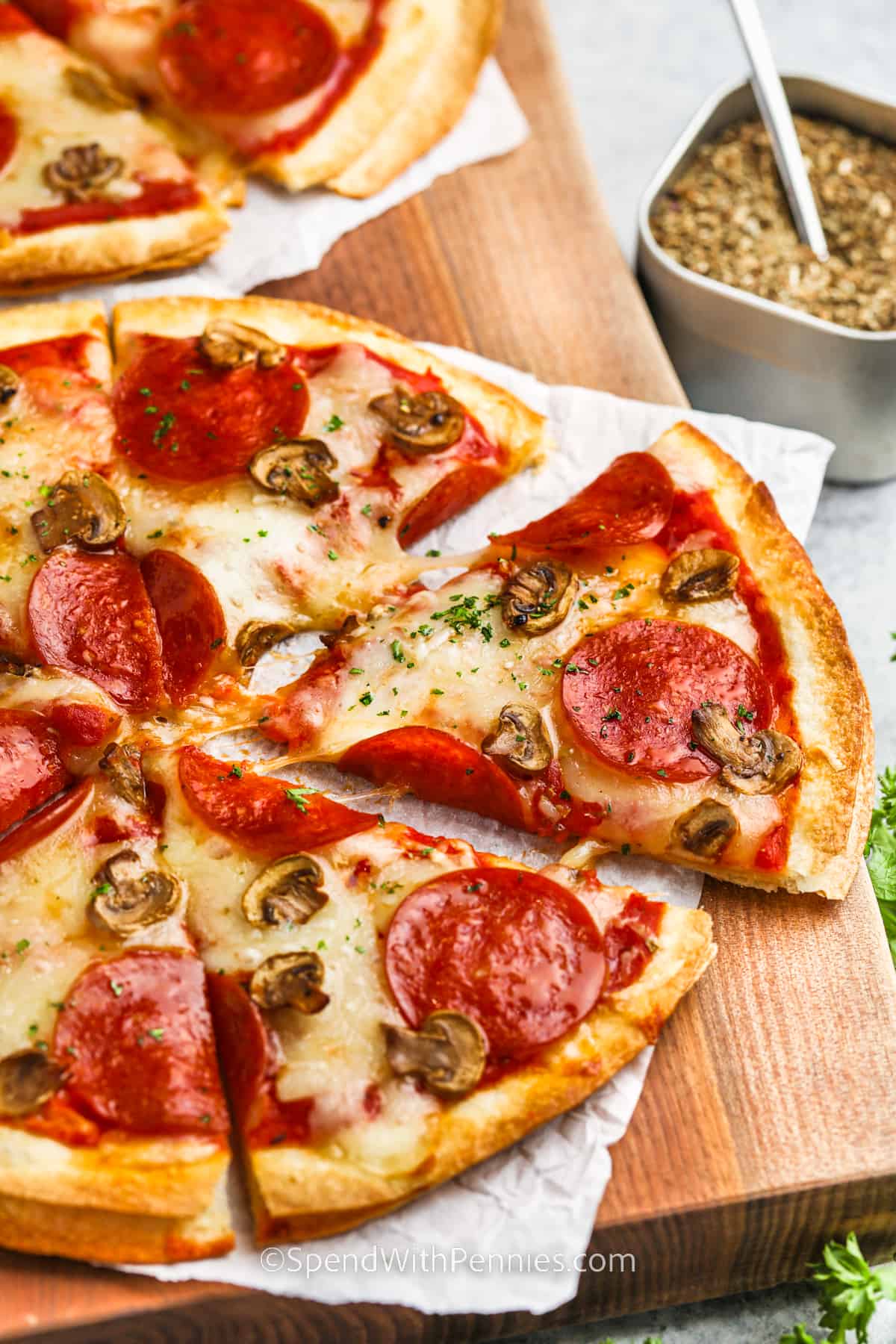 Tortilla pizza is a quick and delicious twist on traditional pizza. Using tortillas as the base, you can easily add sauce, cheese, and your favorite toppings. In just a few minutes, you'll have a crispy personal-sized pizza ready to enjoy. It's a fun and customizable meal for anytime cravings. #tortillapizza #easyrecipe #howtomake #spendwithpennies sliced Tortilla Pizza on a wooden board
