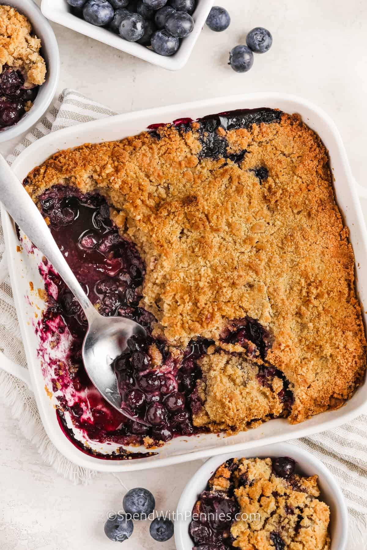 Make a blueberry crumble for a dessert that they won't be able to get enough of. Better than cake, pie, or muffins, this crumble recipe is sure to be the sweet treat of blueberry season. To make it, simply toss some blueberries with sugar, add to a baking dish, top with flour and sugar topping, and then bake until golden and bubbling. #blueberrycrumble #blueberrycrumblerecipe #berrycrumble #spendwithpennies taking a spoonful of Blueberry Crumble out of the dish