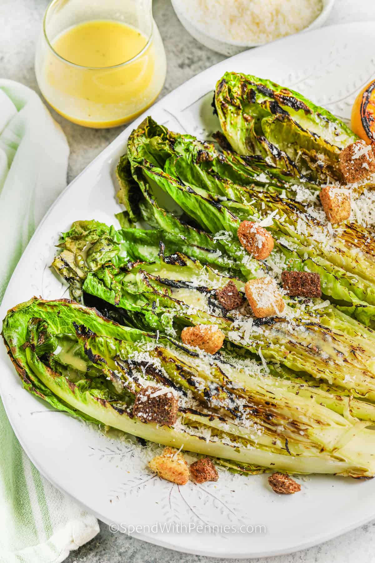 This recipe is a quick and easy way to make grilled romaine on the BBQ. Turn that healthy head of romaine lettuce into flavorful smoky grilled romaine salad with this easy to make recipe. Slightly charred on the BBQ and then drizzled with a tangy vinaigrette, and topped with croutons and parmesan cheese, the summer salad has never tasted this good! #grilledromaine #grilledromainelettuce #grilledromainesalad #spendwithpennies plated Grilled Romaine