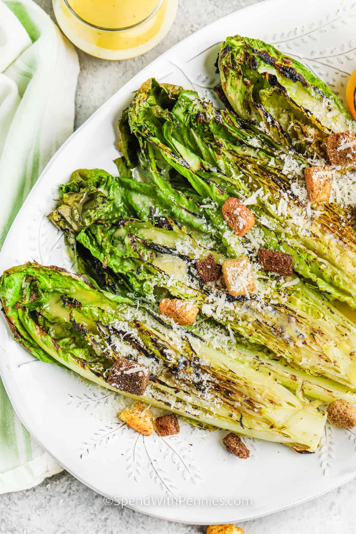 Add a new twist to the summer salad with this grilled romaine recipe. A few minutes on the BBQ or in the oven are all that is needed for this grilled romaine salad. Cut the romaine heart in half, grill, and then drizzle with some lemon, parmesan cheese, and a homemade dressing. Add some crumbled bacon or use a Caesar dressing instead of the vinaigrette. #grilledromaine #grilledromainelettuce #grilledromainesalad #spendwithpennies Grilled Romaine with croutons and parmesan