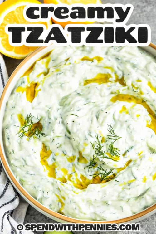 This easy Greek tzatziki recipe is the best sauce to use on anything from chicken to burgers, to fish. It's great on homemade lamb gyros or anything the heart desires. It can even make a great salad dressing. Tzatziki is a versatile sauce that works with so many dishes, with its cool and creamy, tangy flavor profile. #tzatzikirecipe #tzatiki #easy #spendwithpennies bowl of Easy Tzatziki Recipe and lemons beside it with a title