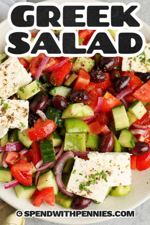 A simple Greek salad is just what is needed for the menu tonight. Summer is the time for simple meals like cold and tangy salads. Plump tomatoes are so delicious when they are served with a tangy dressing and some extra vegetables like cucumber and red onions. Add plenty of feta cheese and some cold salami for protein, and dinner is made! #greeksalad #salad #greekdressing #spendwithpennies bowl of Greek Salad with feta and a title