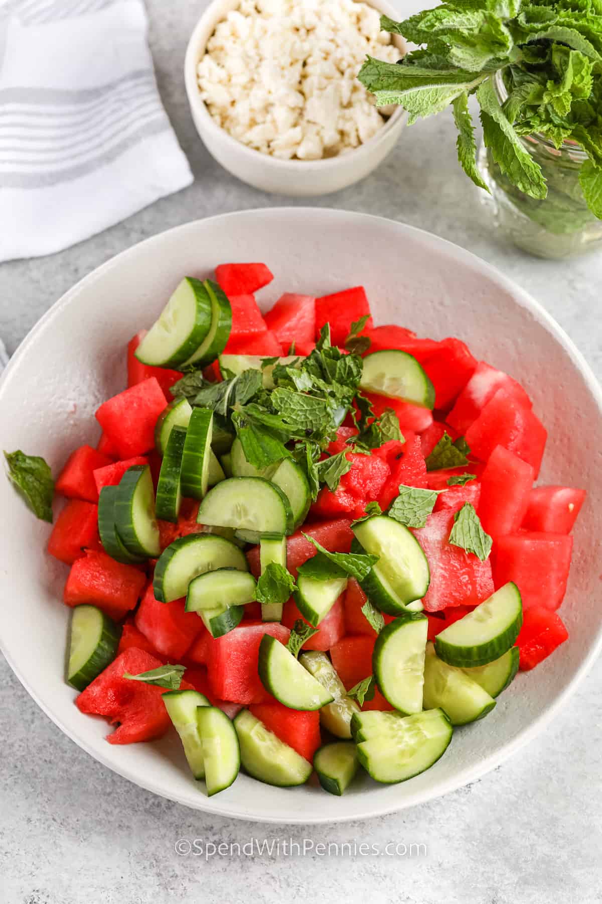 Watermelon salad is easy to make and it has just 5 simple ingredients. Pick a good watermelon that is heavy, and has a yellow patch on it to indicate it's ripe. Try tapping on it to make sure it has a hollow sound. Then just slice it up, chop it into cubes, and toss it with lime juice, cucumber, and mint, then top it with feta cheese. #watermelonsalad #watermelonfetasalad #watermelonfetamintsalad #spendwithpennies ingredients in bowl to make Easy Watermelon Salad with feta and mint