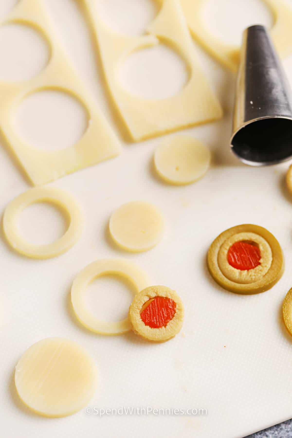 Halloween deviled eggs are a fun, spooky twist on a classic party appetizer. The white of the eggs are marbled with food coloring, and the egg yolk centers have scary spider and eyeball decorations made from olives. You’ll have fun with this crafty recipe and the kids will get a big kick out of making and eating them. Decorate with your own ideas for scary fun. It’s a great eye catching make-and-take snack for costume parties and Halloween gatherings of any kind. #spendwithpennies cutting olives to make Halloween Deviled Eggs