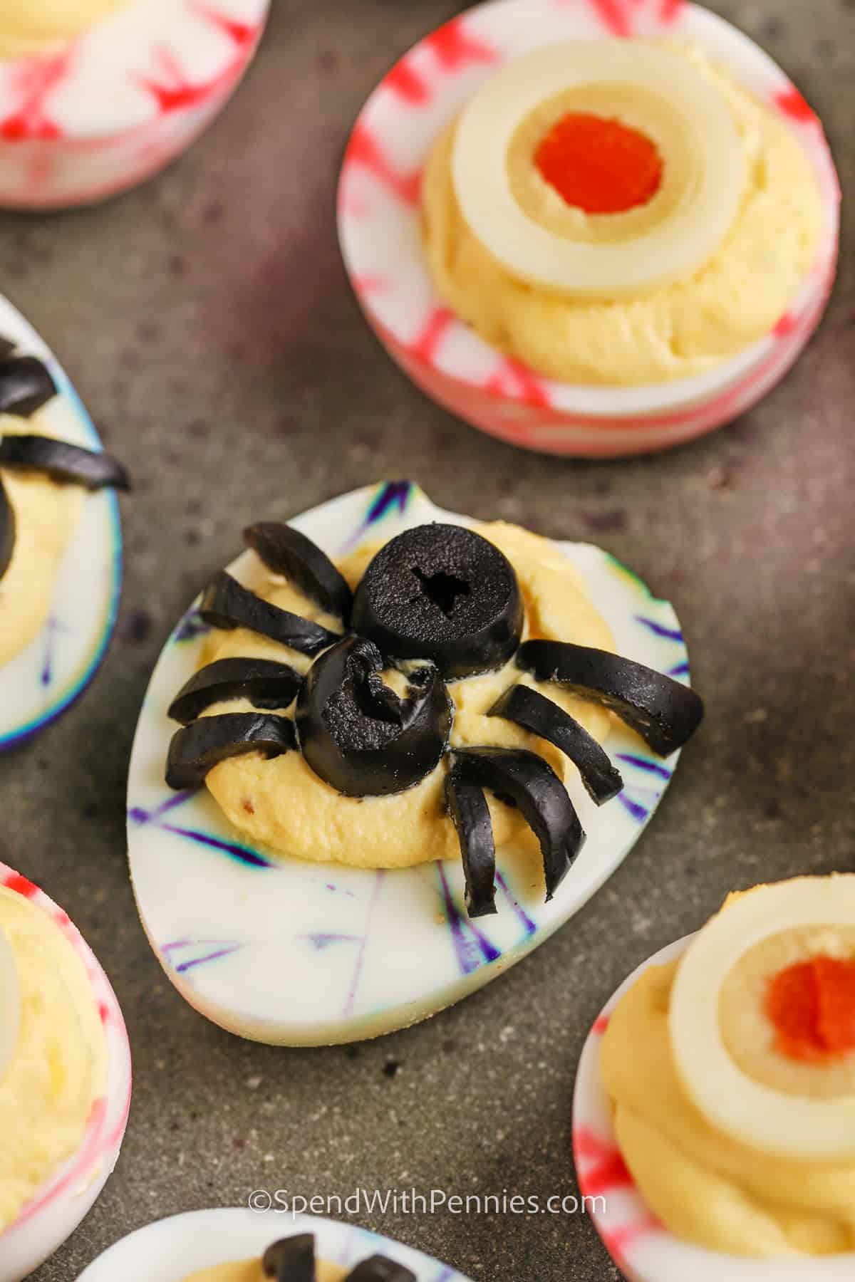 Halloween deviled eggs are a fun, spooky twist on a classic party appetizer. The white of the eggs are marbled with food coloring, and the egg yolk centers have scary spider and eyeball decorations made from olives. You’ll have fun with this crafty recipe and the kids will get a big kick out of making and eating them. Decorate with your own ideas for scary fun. It’s a great eye catching make-and-take snack for costume parties and Halloween gatherings of any kind. #spendwithpennies colorful Halloween Deviled Eggs