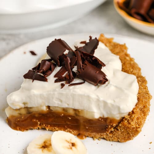 piece of Banoffee Pie on a white plate with banana slices on the side