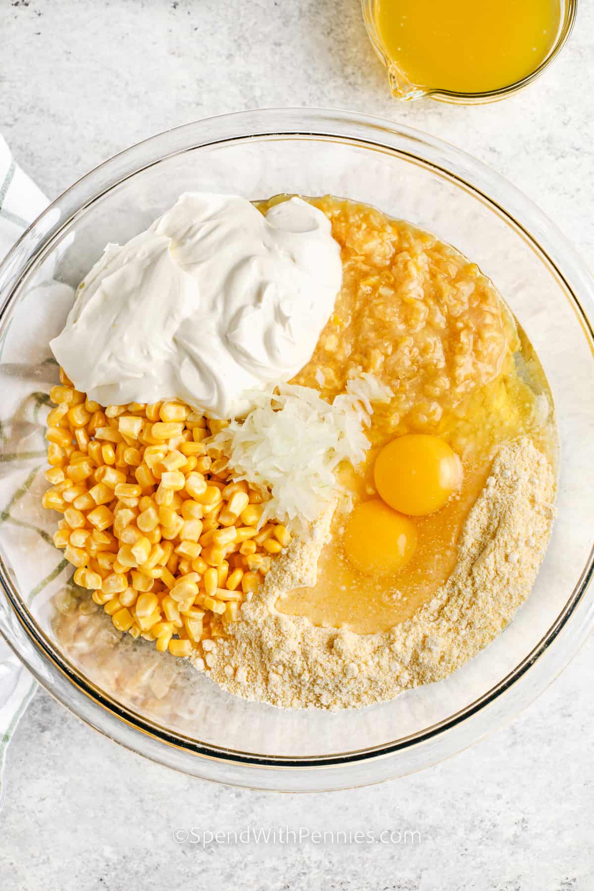Make an easy to make recipe like this crockpot corn casserole for the holidays. Creamy sour cream, sweet corn kernels, and an already prepared box of Jiffy Muffin Corn mix are all it takes to make this simple side dish. For added variation top it with some bacon bits, or crispy cornflakes. #crockpotcorncasserole #corncasseroleinthecrockpot #recipe #spendwithpennies adding ingredients together to make Crockpot Corn Casserole
