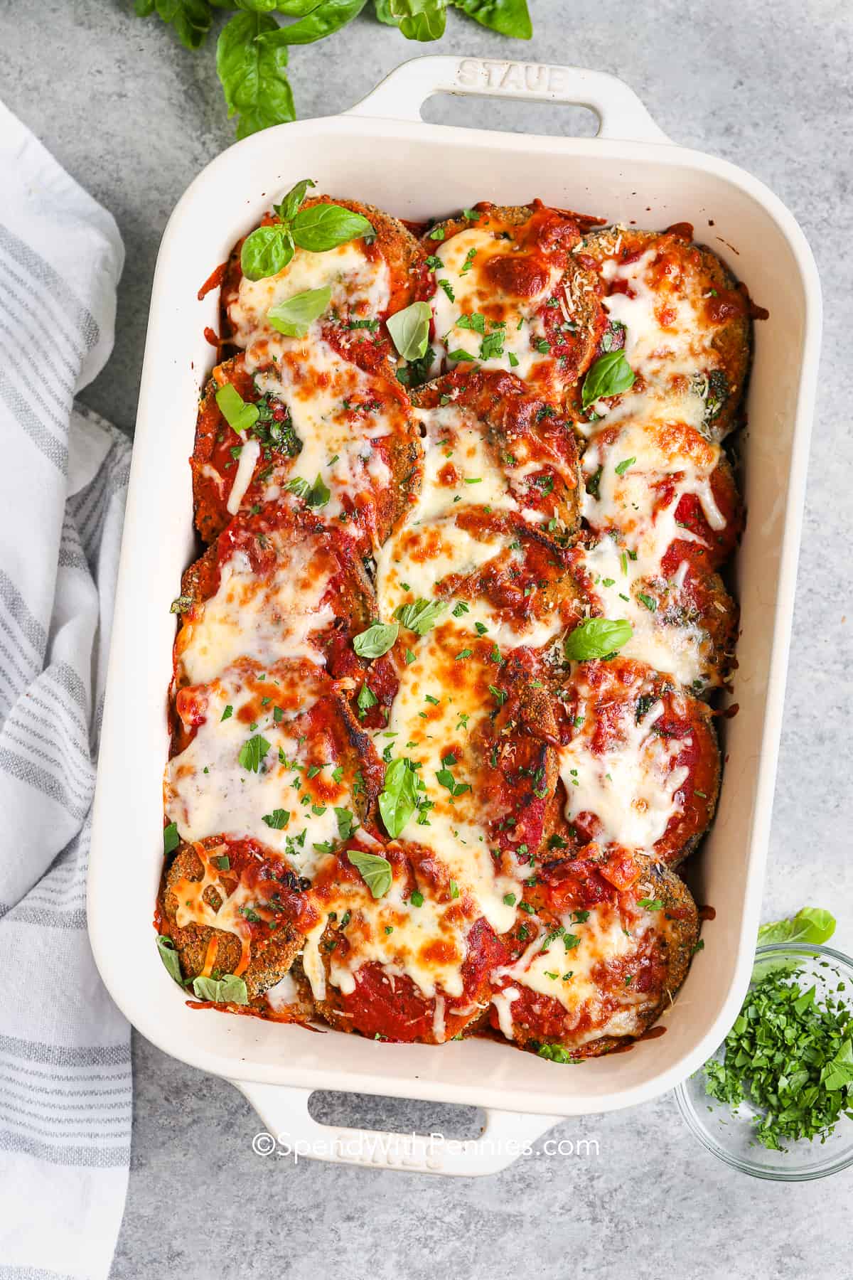 Eggplant parmesan is a classic baked Italian recipe with all the cheesy goodness you crave. Coated slices of eggplant are cooked until crisp, then layered with marinara sauce, herbs, and both mozzarella and Parmesan cheese. This dish is hearty, flavorful, and the best way to enjoy classic Italian comfort food, vegetarian style. Serve it alongside pasta or enjoy it as the star of the meal. Easy to make and always a crowd-pleaser, it’s a favorite for good reason. #spendwithpennies Eggplant Parmesan in a casserole dish with basil as garnish