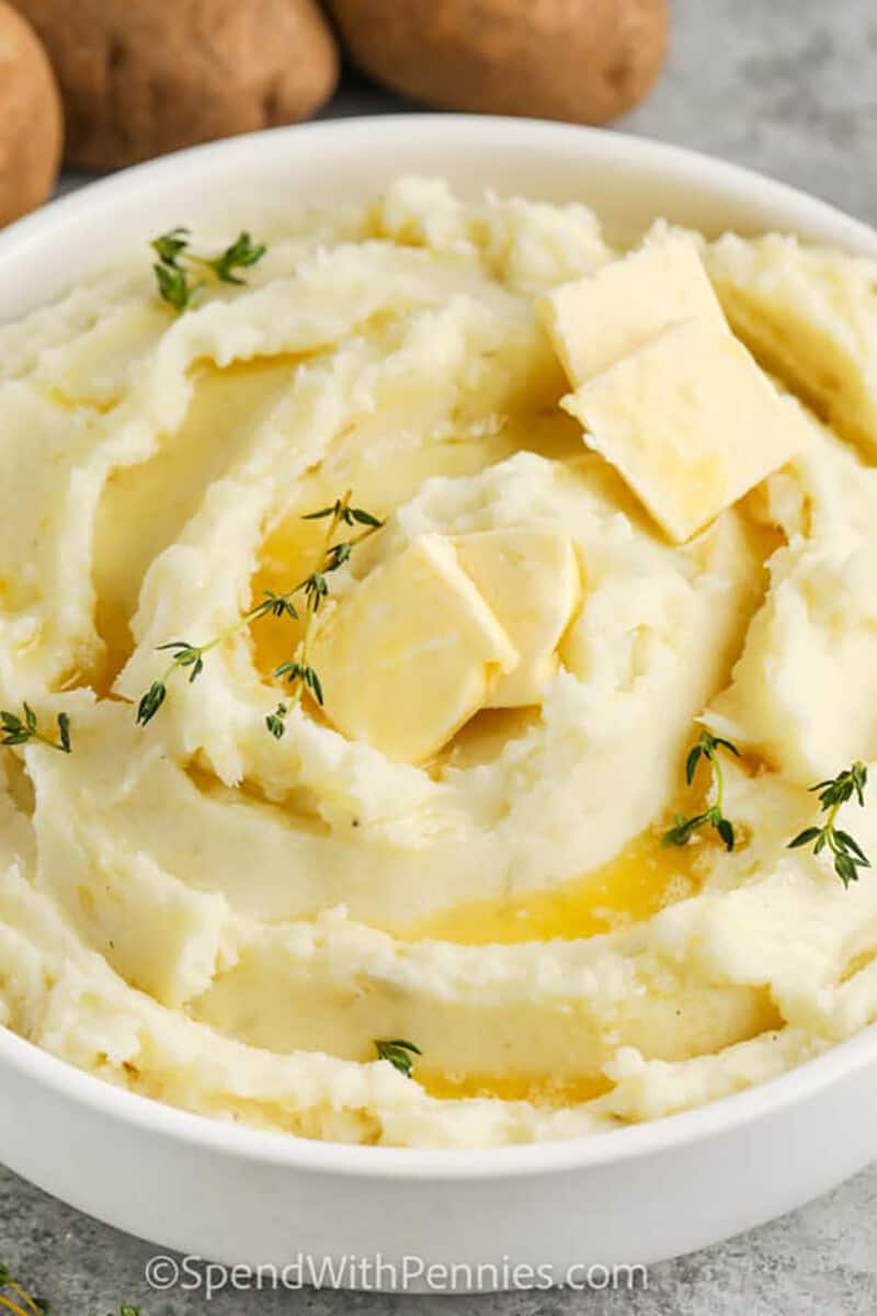 mashed potatoes with butter and thyme on top in a white bowl
