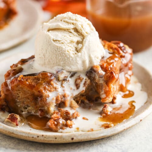 piece of pumpkin bread pudding on a plate with a bite taken out and a scoop of ice cream