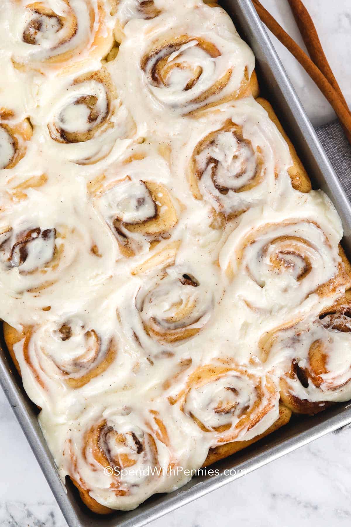 This easy cinnamon roll recipe uses simple ingredients to create soft, airy rolls with a sweet cinnamon-sugar swirl. The dough is smooth and workable, rising into perfect spirals that bake into golden, tender pastries. Spread with a rich cream cheese frosting, they make a comforting breakfast or dessert. Prepare them ahead or enjoy them fresh for a warm treat packed with cinnamon flavor. #spendwithpennies a pan of homemade cinnamon rolls with cream cheese frosting