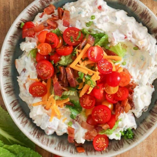 a bowl of BLT dip topped with tomatoes, bacon, lettuce and cheddar cheese