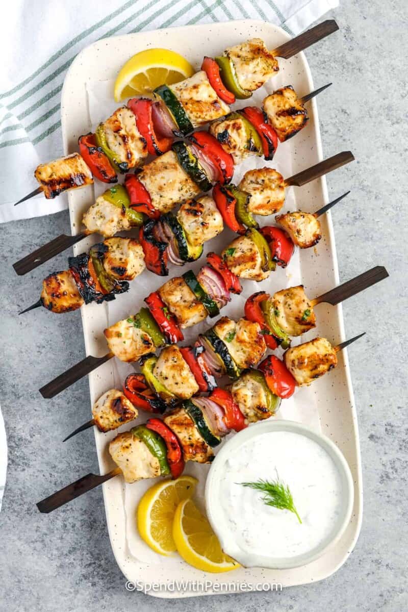 Grilled chicken kabobs with red peppers and zucchini on wooden skewers, served with lemon and dill sauce.