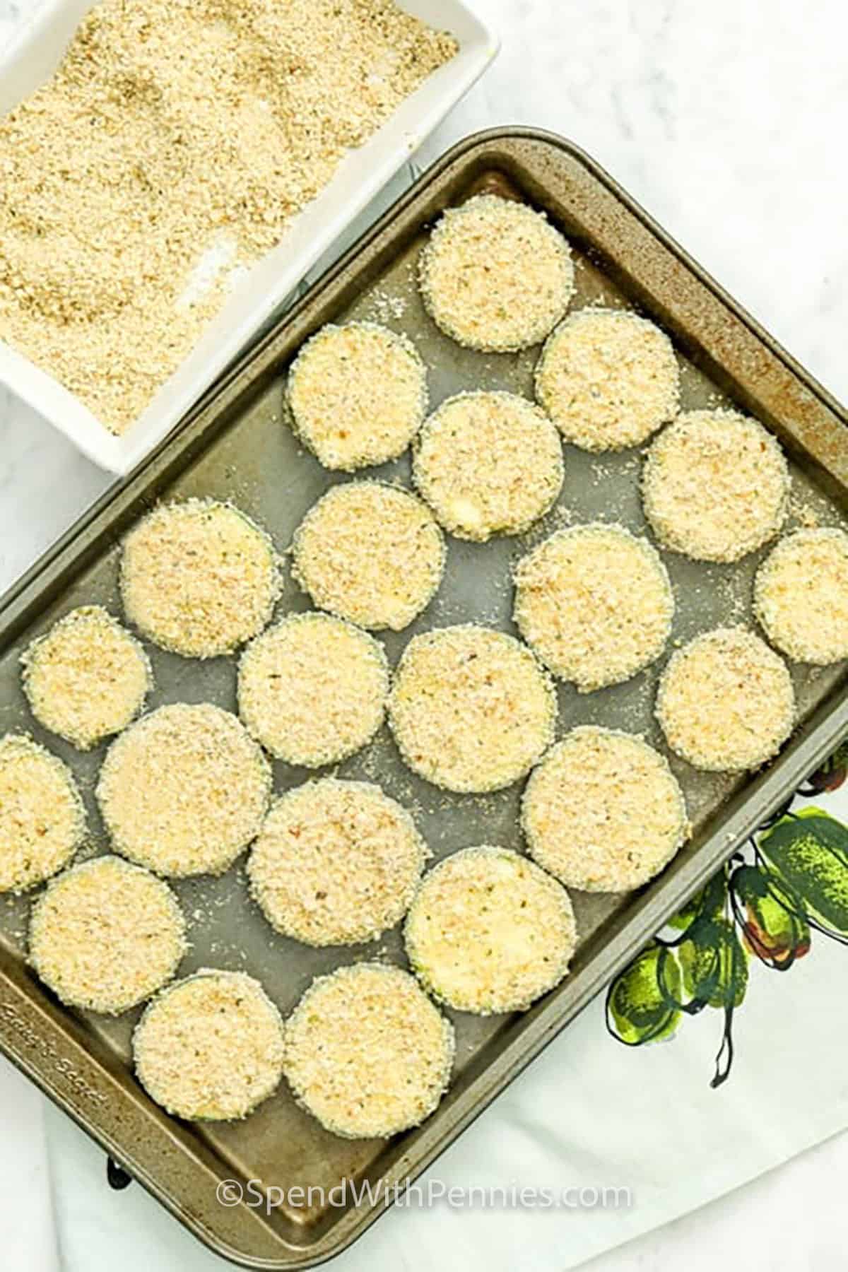 Air fryer fried zucchini is a handy option when you want crispy zucchini bites without pan-frying. The zucchini slices are coated in parmesan breadcrumbs, placed in a single layer, and cooked until golden and crisp. This version is great for easy snacking, summer side dishes, or serving with sandwiches, pasta, and simple weeknight dinners. #spendwithpennies adding coated zucchini bites to sheet pan to make Crispy Fried Zucchini