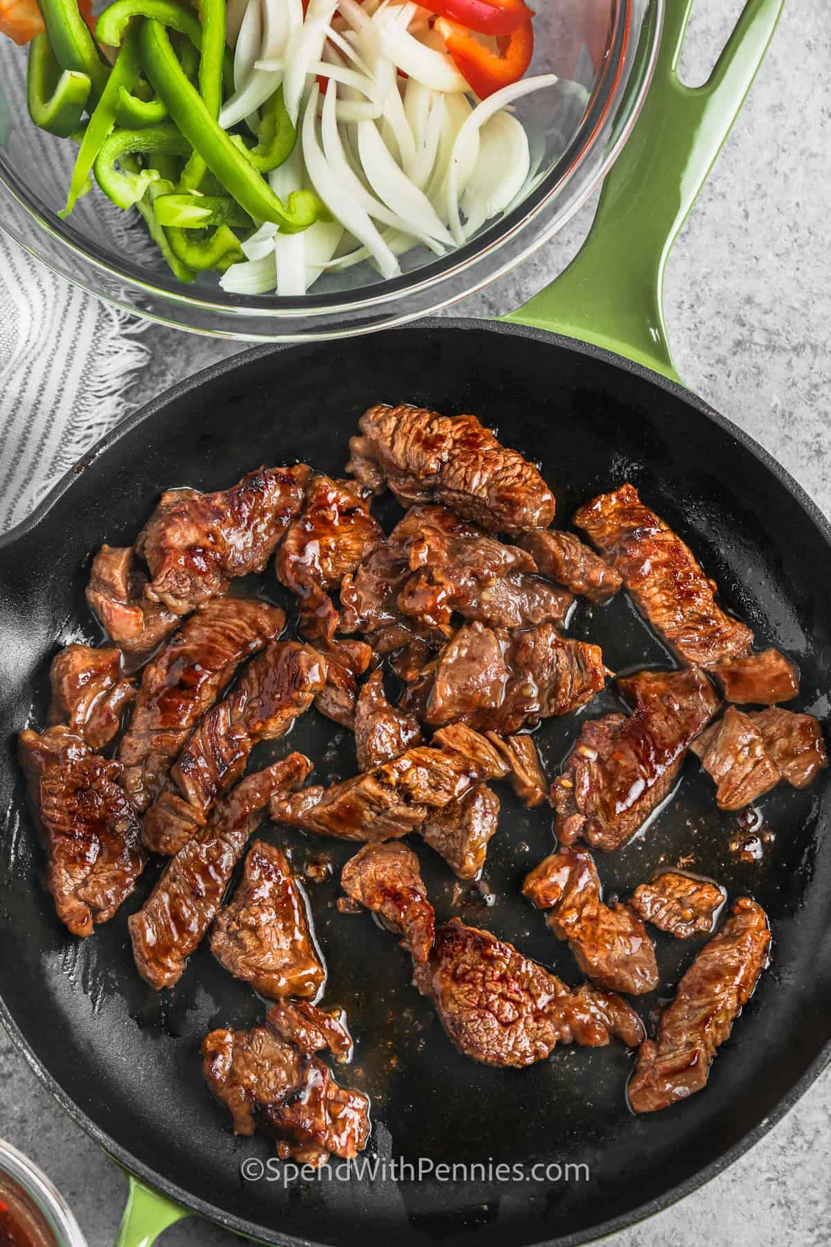 This beef pepper steak recipe is a one-skillet meal with marinated steak, sweet peppers, onions, and a glossy homemade sauce. Slicing the beef thinly against the grain helps keep it tender, while the reserved marinade becomes the rich sauce. Serve this easy pepper steak with rice, fried rice, or noodles for a filling dinner everyone will love. #spendwithpennies cooking Easy Pepper Steak in the pan