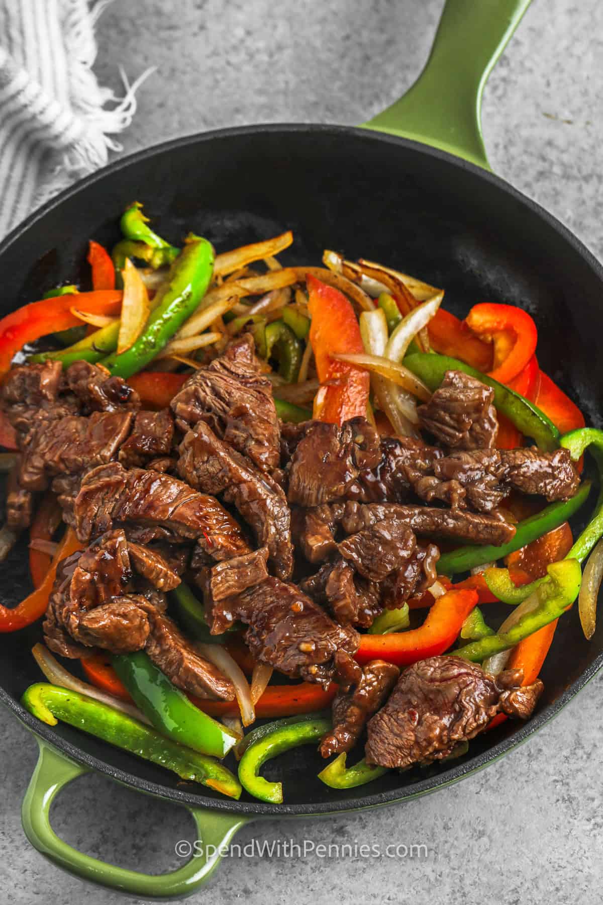 This pepper steak stir fry is packed with tender beef strips, crisp-tender peppers, and a rich garlic ginger sauce. A short marinade helps tonight's round beef become more flavorful, while a hot skillet gives the steak a good sear. Spoon this saucy beef pepper steak over steamed rice for a hearty family dinner with big takeout-style flavor. Pin this recipe for tonight's dinner. #spendwithpennies addin Easy Pepper Steak to peppers and onions in the pan