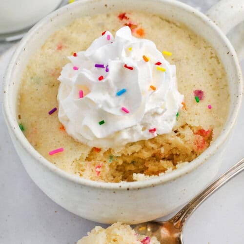 Vanilla Mug Cake with whipped cream and sprinkles with a portion taken out
