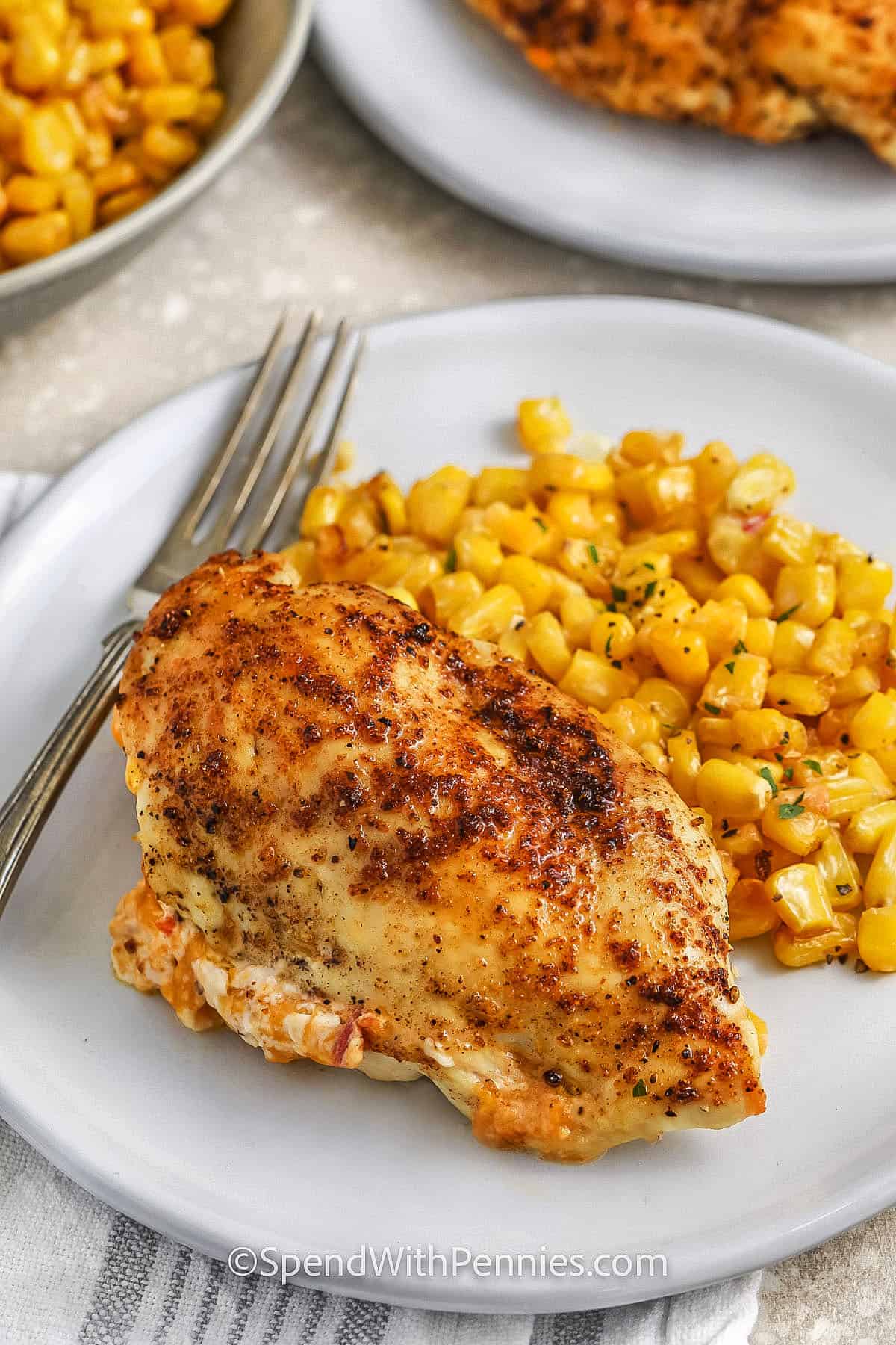 Air fryer pimento stuffed chicken breasts are a flavorful and easy meal. Juicy chicken breasts are filled with a rich mixture of cream cheese, sharp cheddar, and chopped pimentos, then seasoned with paprika and garlic. Cooked to perfection in the air fryer, these stuffed chicken breasts are tender and delicious. Serve them with sweet and buttery honey corn, which is cooked right in the air fryer for a simple yet satisfying side dish. Perfect for a quick weeknight dinner! #spendwithpennies plated dish of Air Fryer Pimento Stuffed Chicken Breasts with corn
