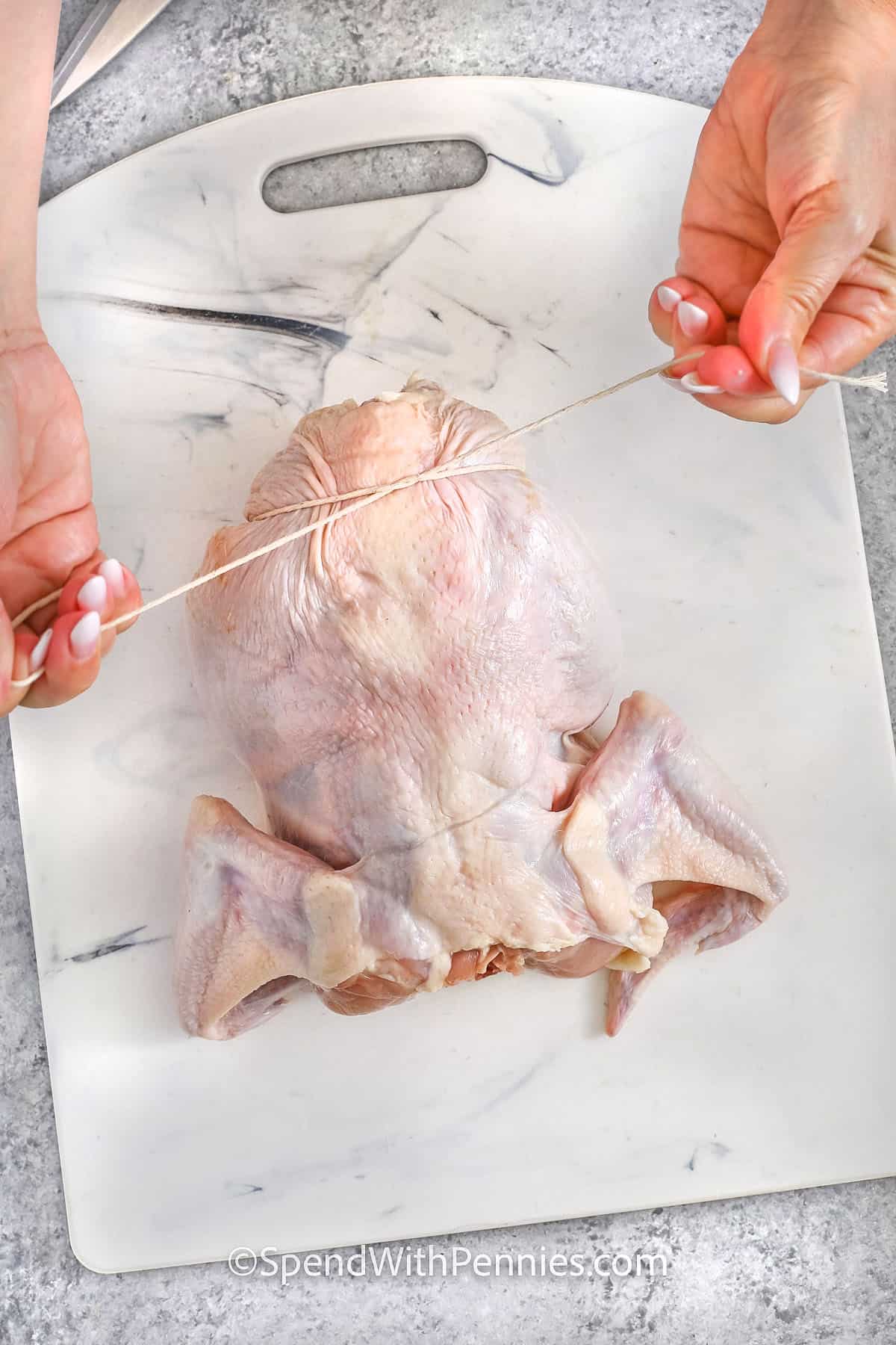 Roasting a whole chicken is one of those simple, comforting meals that always feels special. With just a bit of seasoning and a drizzle of oil, you’ll get that perfectly crispy skin while keeping the meat juicy. Adding an onion inside gives it a subtle, sweet flavor, and trussing the legs helps the chicken cook evenly. After roasting, let it rest so the juices stay locked in. It’s the kind of meal that makes the whole house smell amazing, and it's sure to be a hit with the family! #spendwithpennies tying a chicken with string to show How to Prepare a Whole Chicken