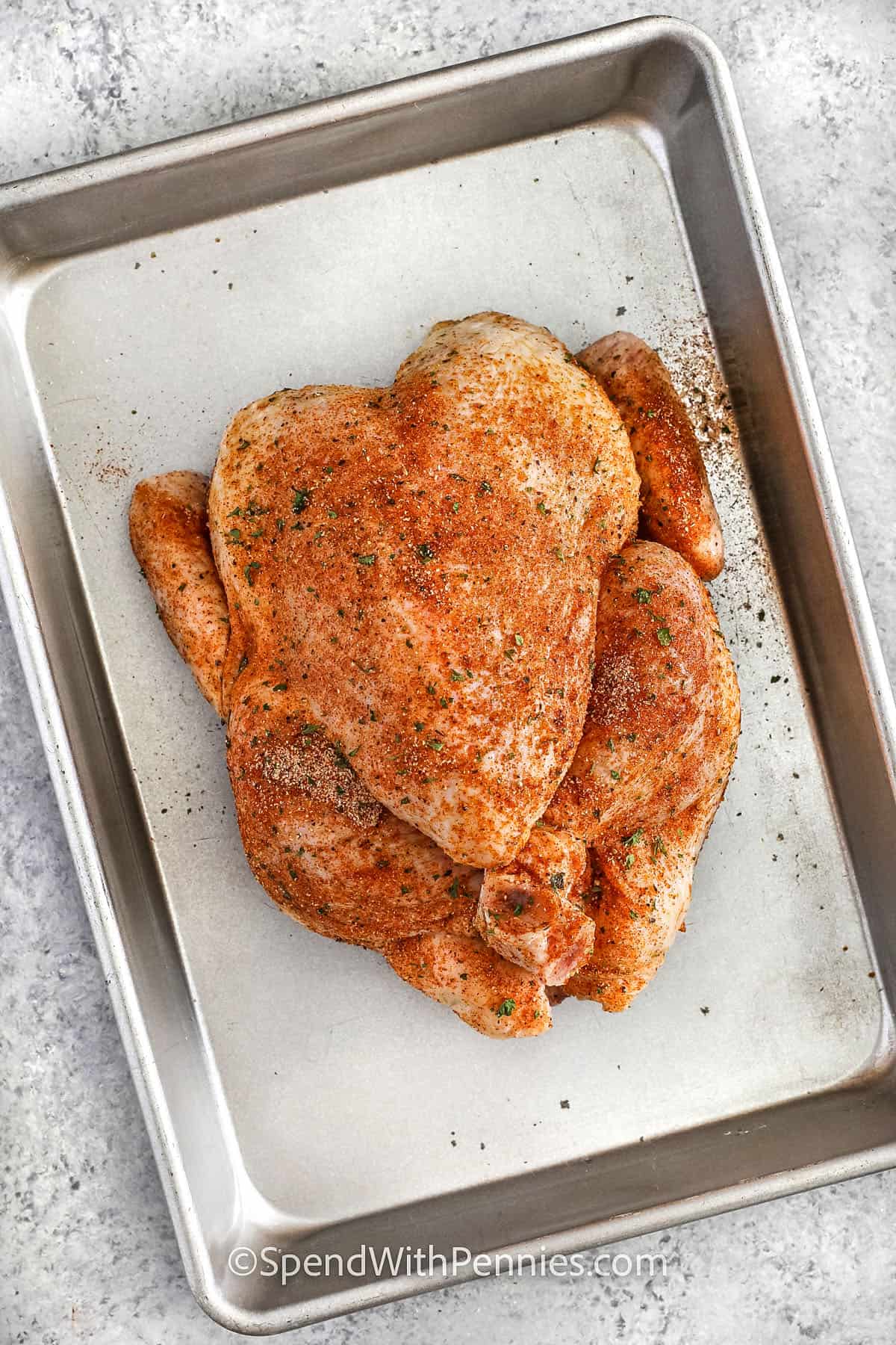 Roasting a whole chicken is one of those classic meals that’s both easy and delicious. A simple rub of oil and seasoning gives you that crispy skin and juicy meat that everyone loves. Adding an onion inside adds just the right touch of flavor, and trussing the legs helps it cook evenly. Letting it rest before carving makes sure it stays tender and flavorful. It's the perfect recipe for a cozy, homemade dinner that the whole family will enjoy! #spendwithpennies seasoned chicken on a sheet pan to show How to Prepare a Whole Chicken