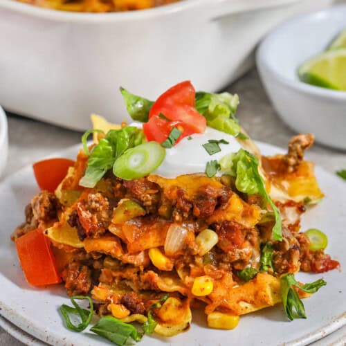 Plated taco bake with toppings and a casserole dish.