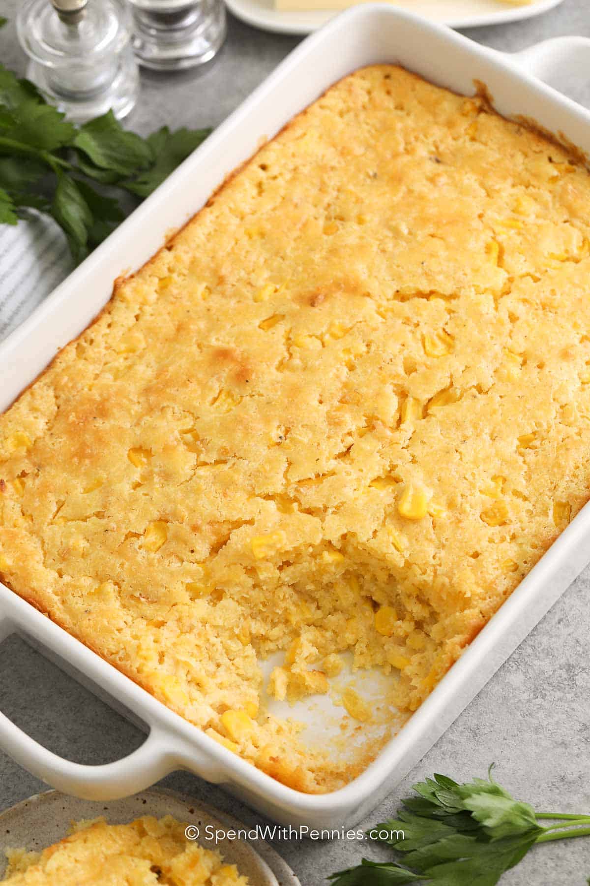 corn casserole in a white baking dish with a scoop taken out of it