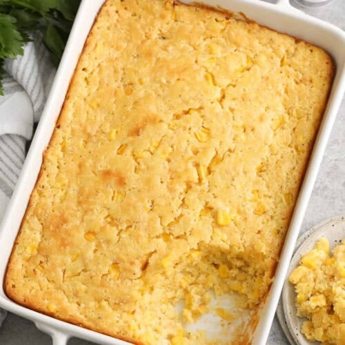 corn casserole in a white baking dish next to parsley and butter