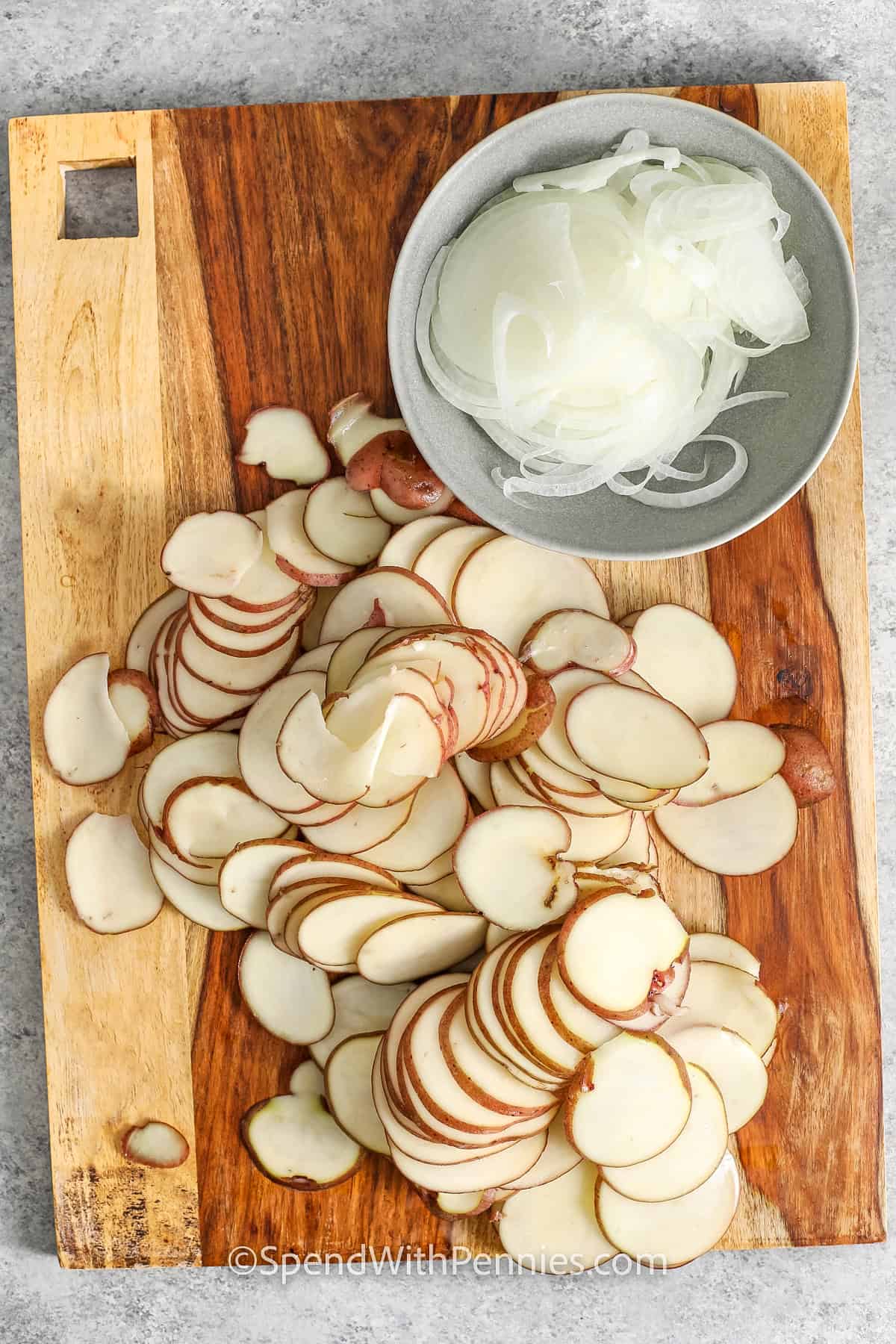 Potatoes au gratin is a rich, cheesy recipe baked to golden perfection. Layers of tender potatoes and onions are covered in a creamy cheese sauce for a side dish that’s pure comfort. This easy recipe is simple to cook and always a hit served with ham, chicken, turkey, or roast beef. #spendwithpennies Sliced potatoes and onions for potatoes au gratin