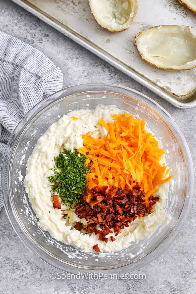 adding cheese bacon and chives to potatoes to make Twice Baked Potatoes