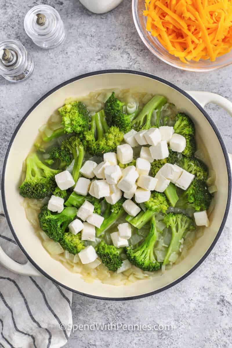 Adding cream cheese cubes to sauteed onions and broccoli to make broccoli cheddar soup.