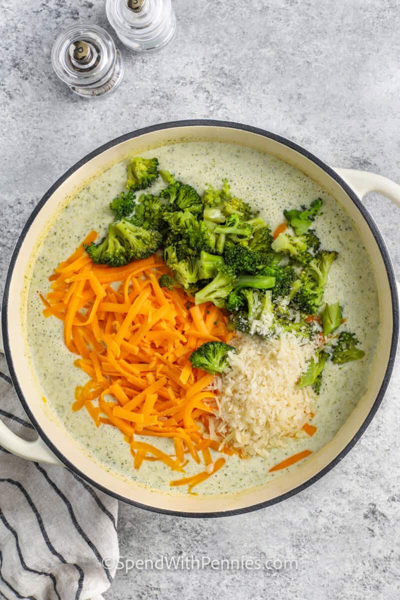 Cheese and broccoli floating on top of a pot of broccoli cheddar soup.