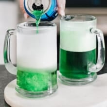 adding beer to top off glasses of green beer on a white platter