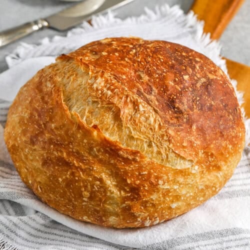 loaf of No Knead Bread on a cutting board and towel