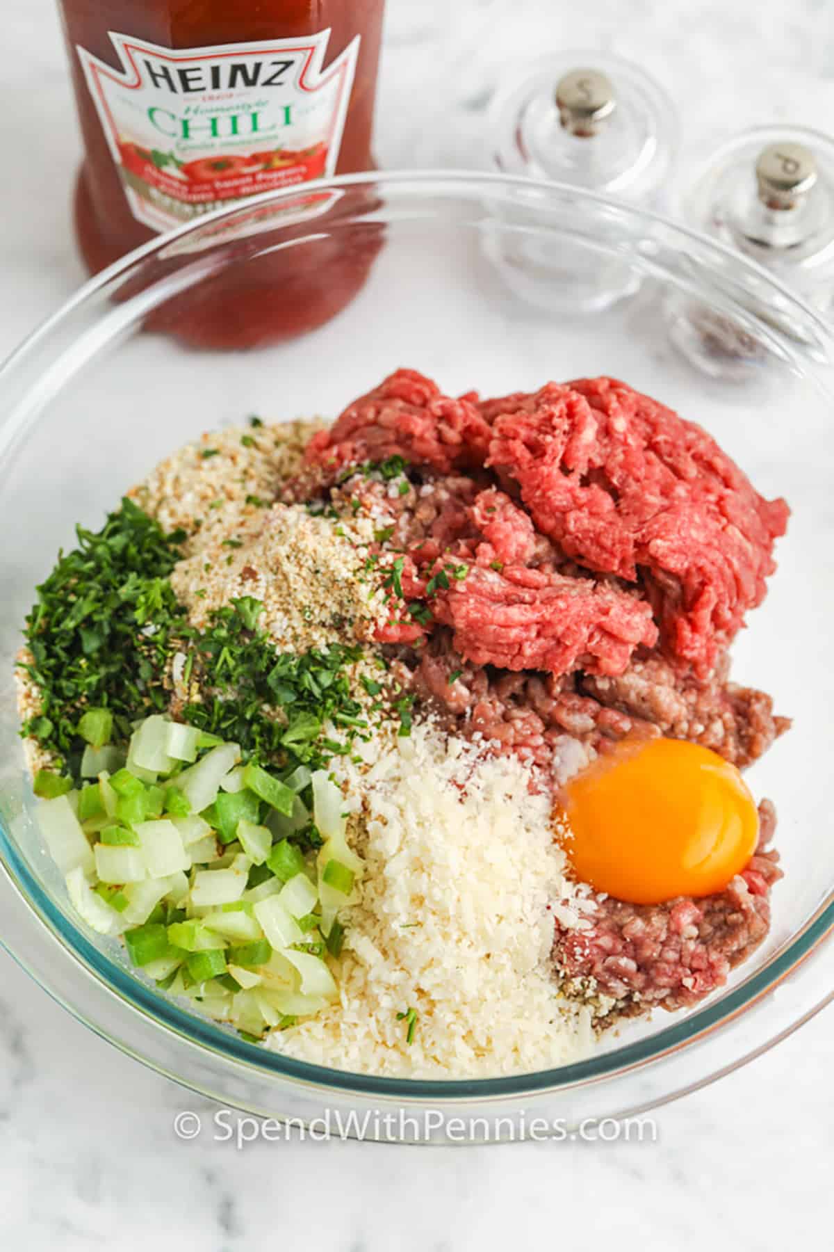 Air fryer meatloaf is the perfect way to enjoy this classic dish in a fraction of the time. Ground beef, bell pepper, onions, breadcrumbs, and a variety of seasonings combine to create a juicy mini meatloaf, while the tomato-chili sauce topping adds the ideal burst of flavor. With a cook time of just 25 minutes, this easy, delicious recipe is perfect for a quick family meal. #spendwithpennies ingredients in a bowl to make Air Fryer Meatloaf